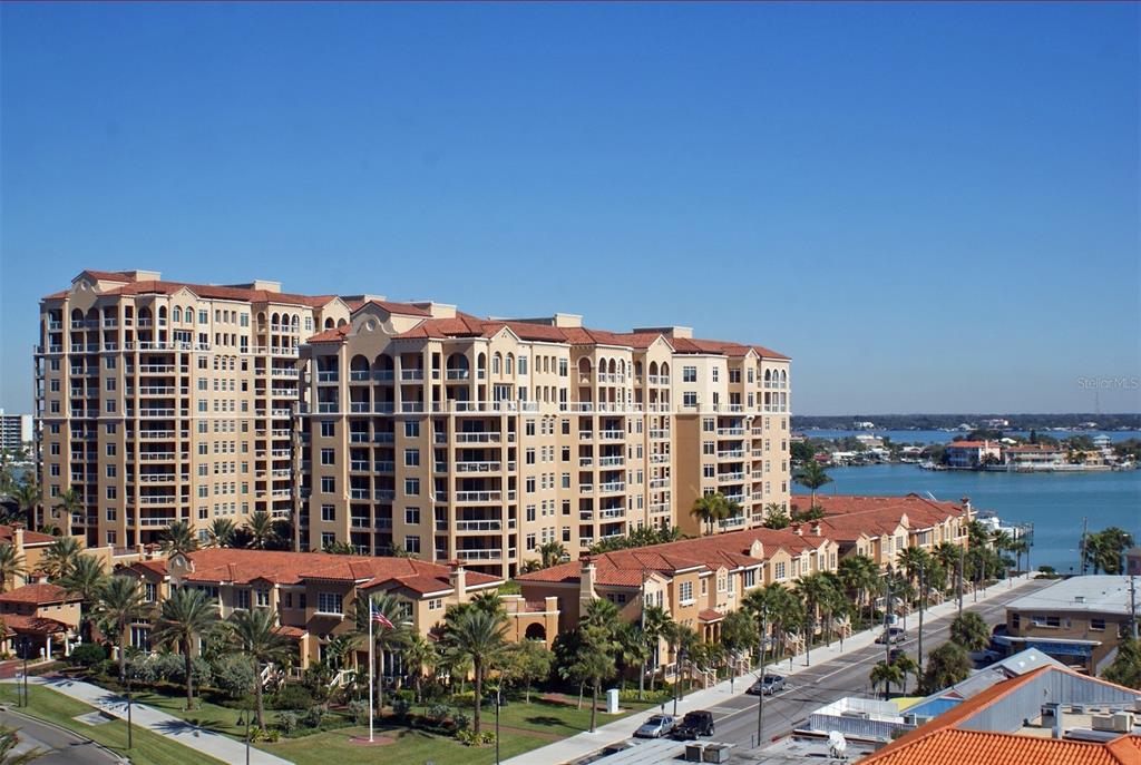 An elevated view of a large multi-story apartment complex with terracotta roofs near water — 521 MANDALAY AVENUE UNIT 704, CLEARWATER BEACH, FL
