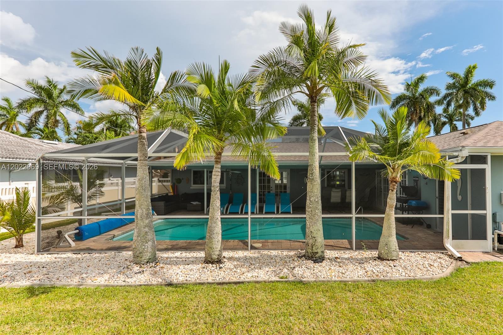 A swimming pool sits inside a screened enclosure behind a house with palm trees — 355 Bayshore Dr, Cape Coral FL 33904, CAPE CORAL, FL
