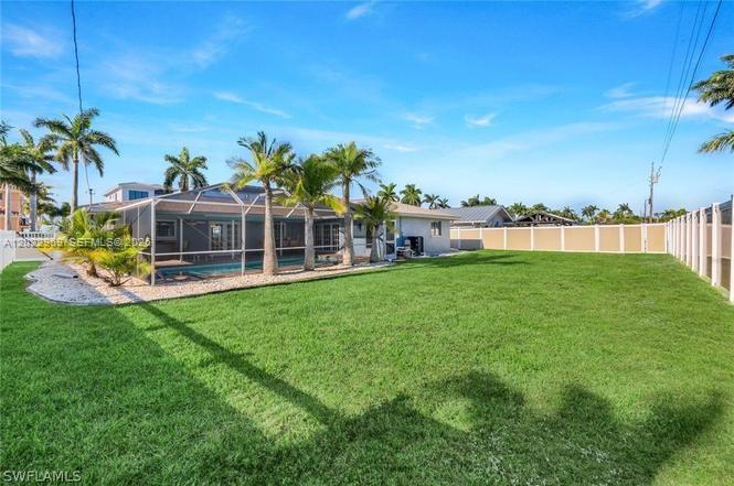A backyard features a screened-in pool, palm trees, and a white fence under a blue sky — 355 Bayshore Dr, Cape Coral FL 33904, CAPE CORAL, FL