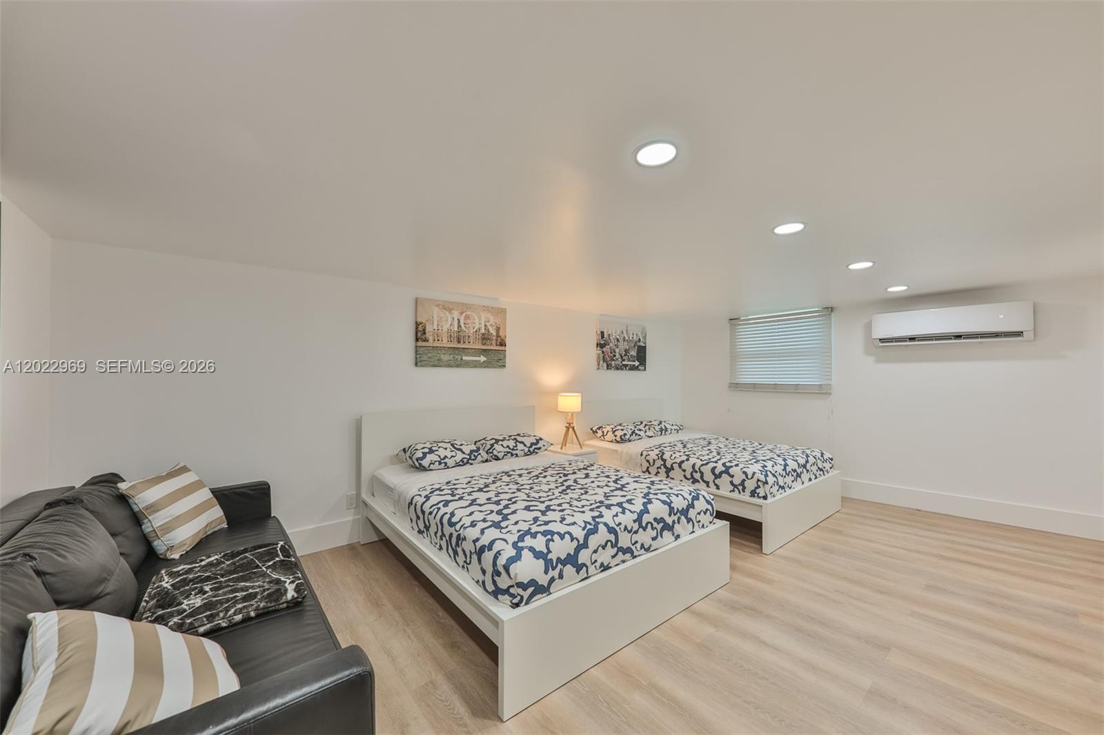 A bedroom features two beds, a dark sofa, light wood flooring, and a wall-mounted AC — 355 Bayshore Dr, Cape Coral FL 33904, CAPE CORAL, FL