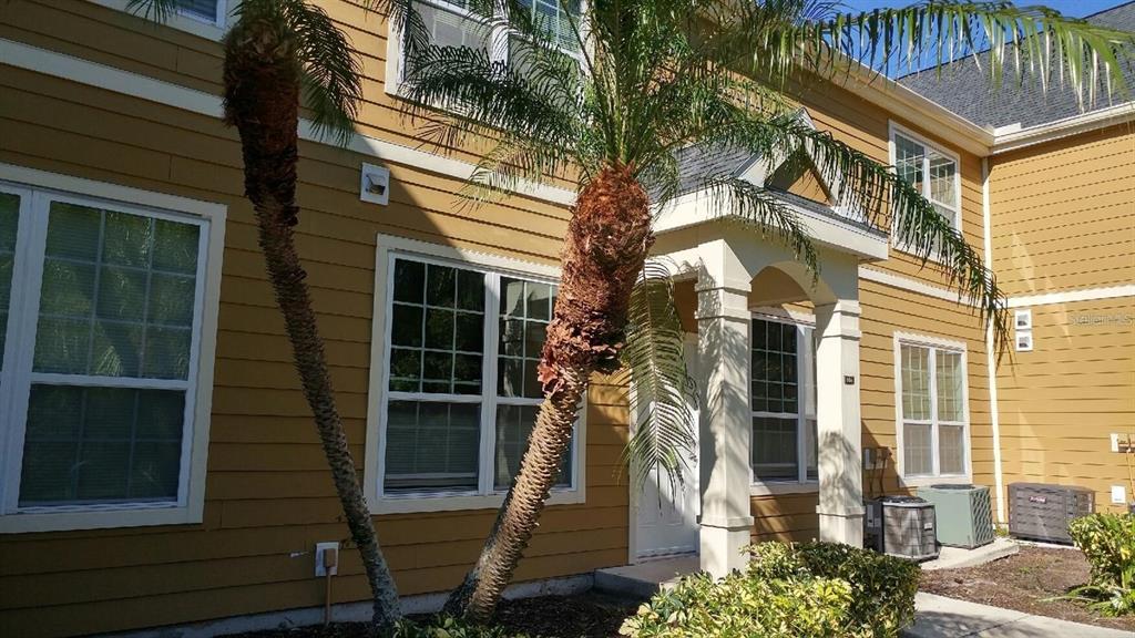 A two-story tan building with a covered entryway, palm trees, and exterior air conditioning units — 5591 ROSEHILL ROAD UNIT 104, SARASOTA, FL