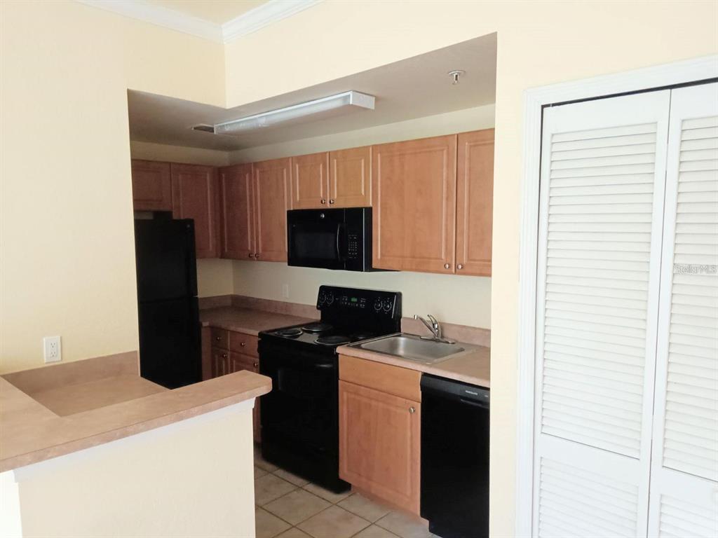 A kitchen features light wood cabinets, black appliances, and a tan countertop — 5591 ROSEHILL ROAD UNIT 104, SARASOTA, FL