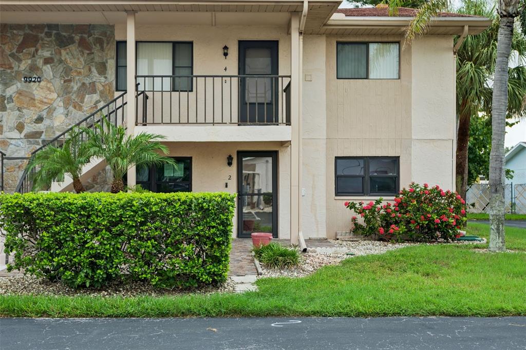 A two-story apartment building exterior features a stone facade, a balcony, and a green hedge — 9920 EAGLES POINT CIRCLE UNIT 2, PORT RICHEY, FL