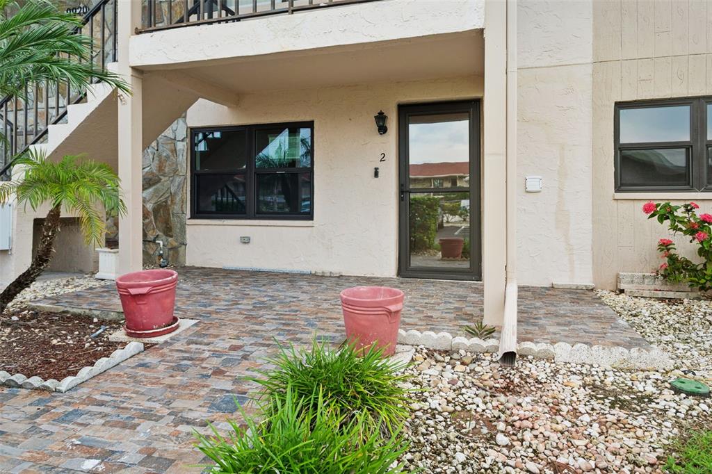 A ground-level patio with stone pavers sits in front of a building entrance with stairs — 9920 EAGLES POINT CIRCLE UNIT 2, PORT RICHEY, FL