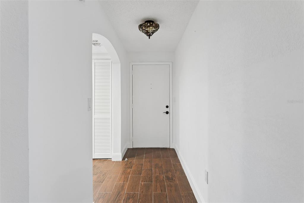 A white entryway features a wooden tile floor, an arched doorway, and a decorative ceiling light — 9920 EAGLES POINT CIRCLE UNIT 2, PORT RICHEY, FL