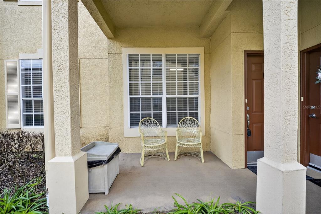 A covered concrete porch features two wicker chairs, a storage bin, and a brown door — 839 GRAND REGENCY POINT UNIT 104, ALTAMONTE SPRINGS, FL