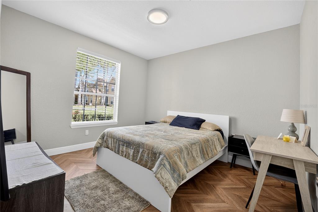A bedroom features a bed, a desk, a mirror, and herringbone-patterned wood flooring — 839 GRAND REGENCY POINT UNIT 104, ALTAMONTE SPRINGS, FL