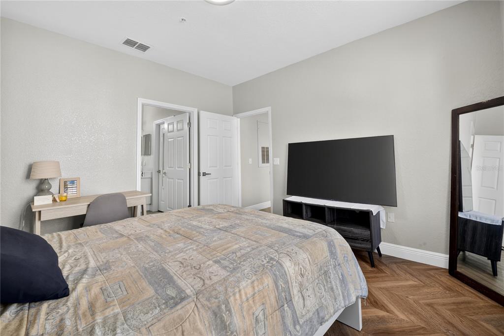 A bedroom features a bed, a desk, a television on a stand, and a floor mirror — 839 GRAND REGENCY POINT UNIT 104, ALTAMONTE SPRINGS, FL