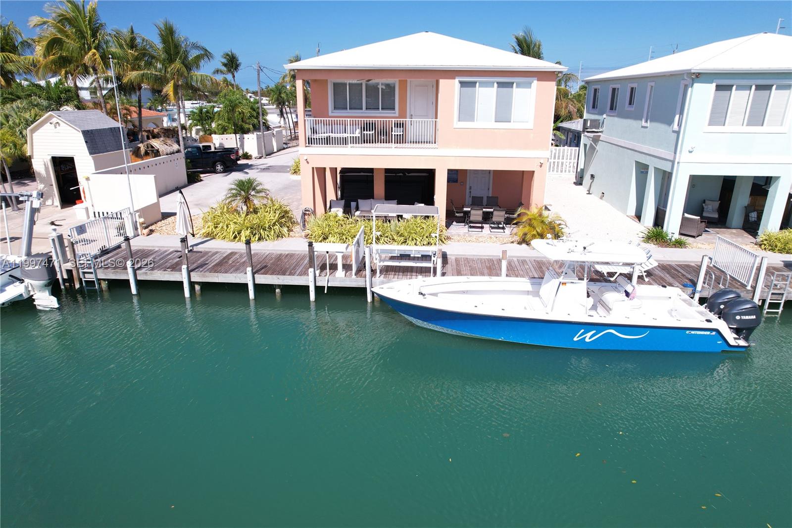 An elevated peach-colored house sits beside a canal with a boat docked in front — 11284 3rd Avenue Ocean, Marathon FL 33050, MARATHON, FL