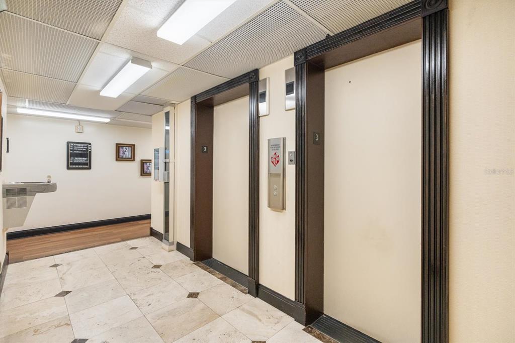 An indoor hallway features two elevator doors with dark wood trim and tiled flooring — 157 E NEW ENGLAND AVENUE UNIT 302, WINTER PARK, FL
