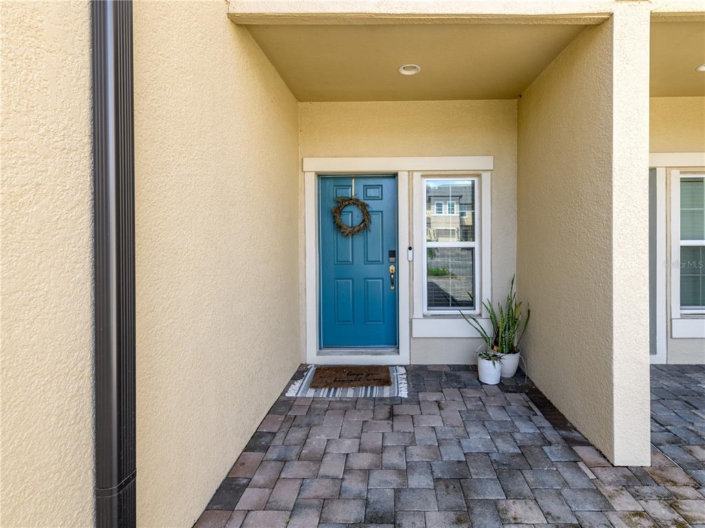 A blue front door with a wreath sits under a covered entryway with paver flooring — 29844 SOUTHWELL LANE, WESLEY CHAPEL, FL
