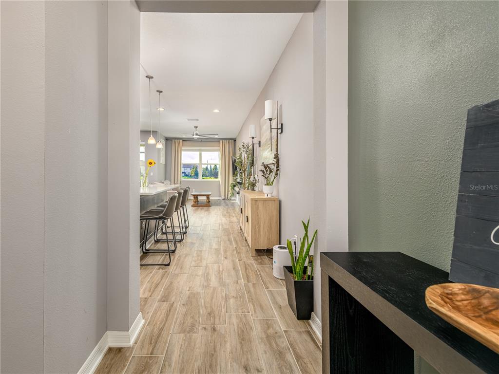 A hallway with wood-look tile flooring leads into an open-concept kitchen and living area — 29844 SOUTHWELL LANE, WESLEY CHAPEL, FL