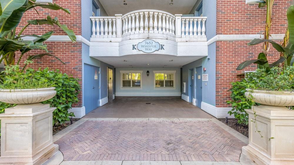 A brick building exterior features a covered entryway with a balcony and large stone planters — 7652 WHISPER WAY UNIT 104, REUNION, FL