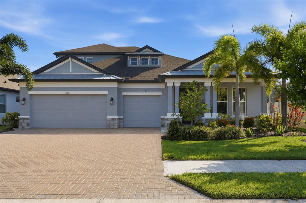 A gray single-story house with a paved driveway, a three-car garage, and palm trees — 5542 NATIVE HENNA COURT, SARASOTA, FL