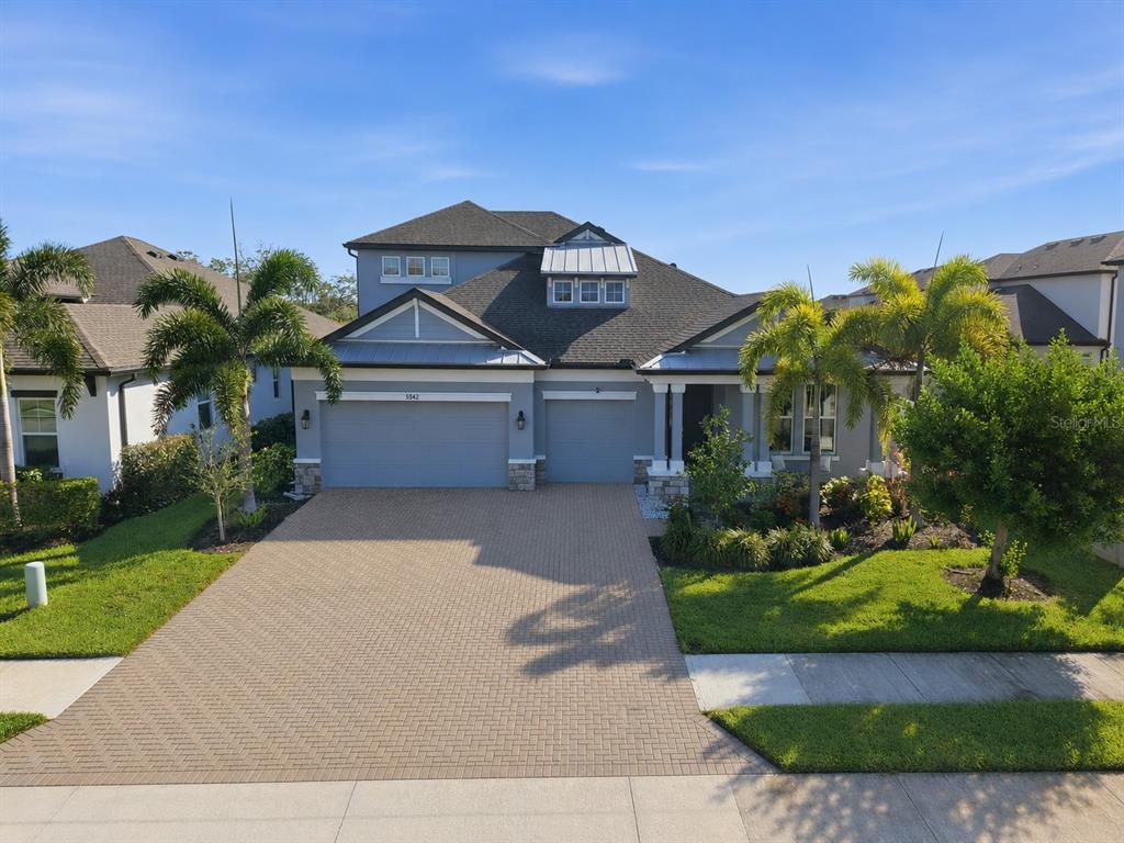 A two-story gray house with a paver driveway and a three-car garage — 5542 NATIVE HENNA COURT, SARASOTA, FL