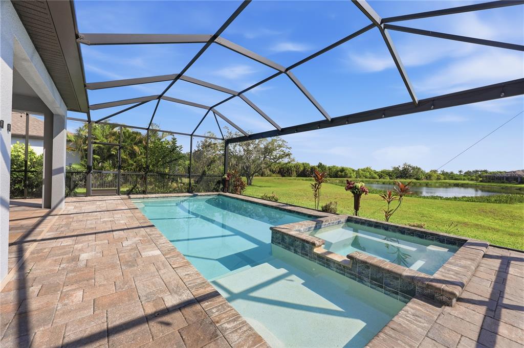 A screened-in swimming pool and spa overlook a grassy lawn and a pond — 5542 NATIVE HENNA COURT, SARASOTA, FL