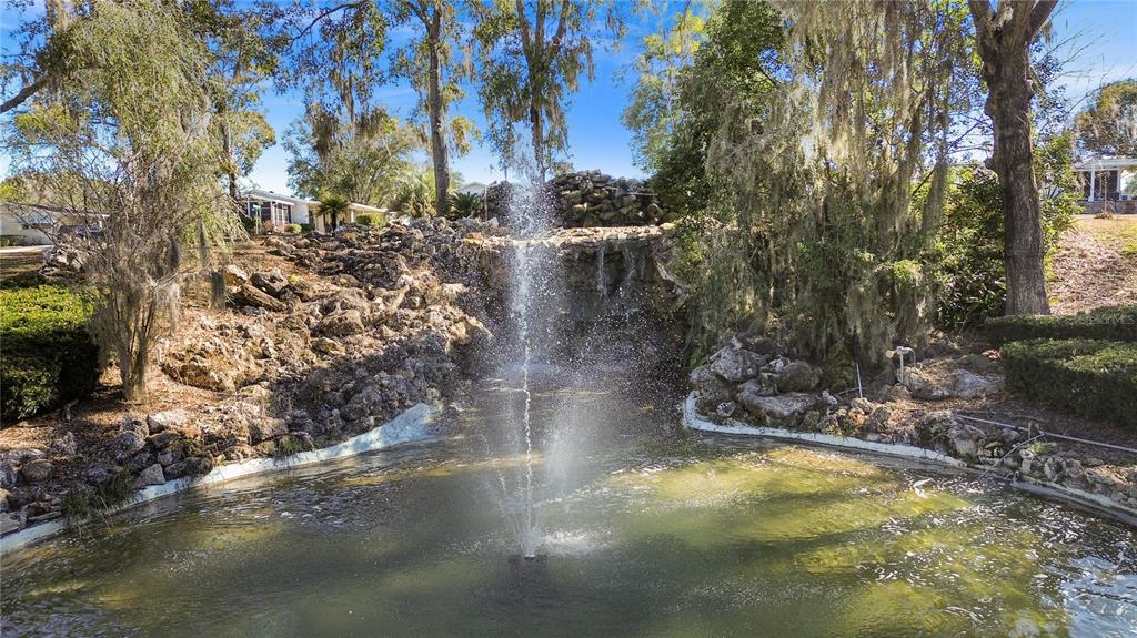 A fountain sprays water into a pond surrounded by a rocky landscape and trees — 7964 SW 6TH PLACE, OCALA, FL
