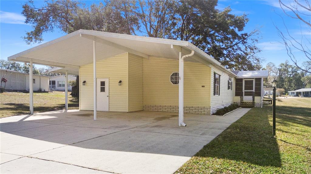 A yellow mobile home features a large attached carport and a concrete driveway — 7964 SW 6TH PLACE, OCALA, FL