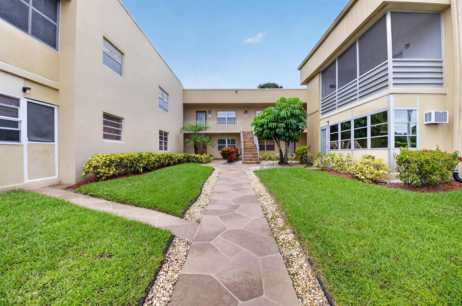 A stone walkway leads through a grassy courtyard between two multi-story apartment buildings — 506 E Capri Road # 506, Delray Beach FL 33484, DELRAY BEACH, FL