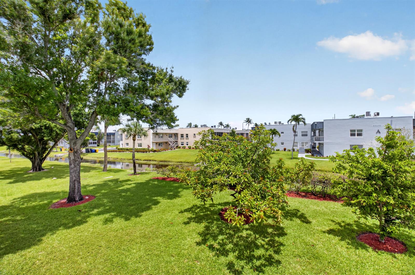 A grassy lawn with trees and a small pond in front of apartment buildings — 506 E Capri Road # 506, Delray Beach FL 33484, DELRAY BEACH, FL
