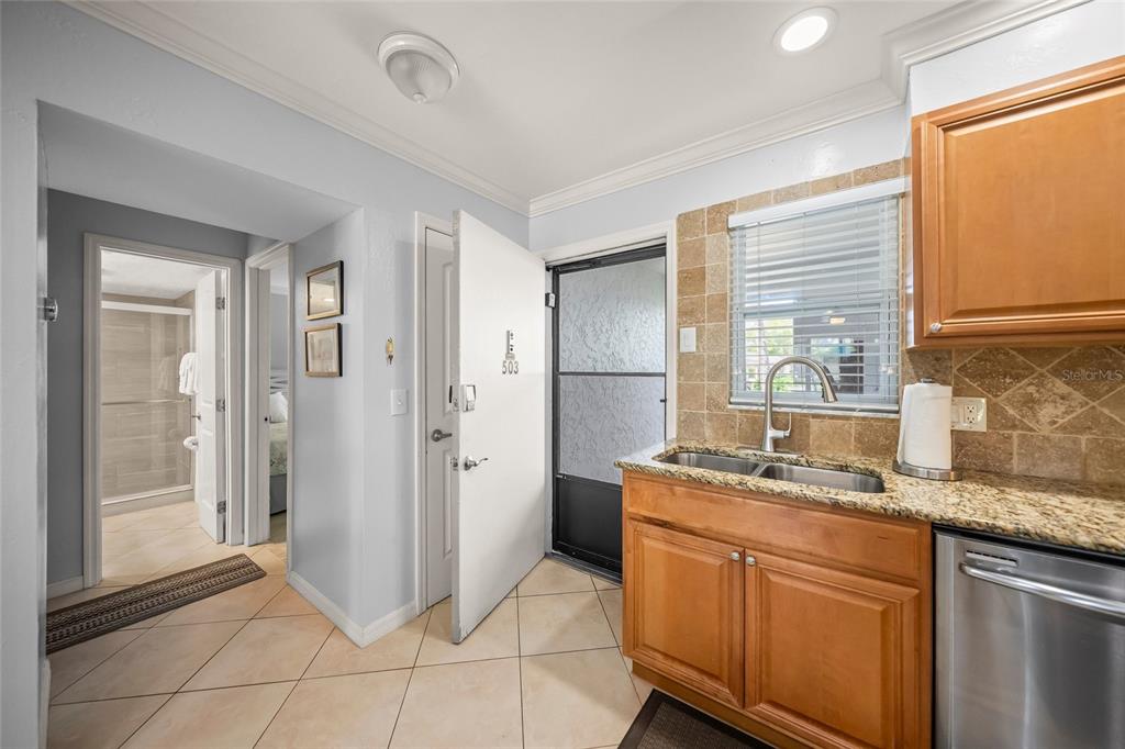 A kitchen with wooden cabinets, granite countertops, and a stainless steel dishwasher near an entryway — 5619 MIDNIGHT PASS ROAD UNIT 503, SARASOTA, FL