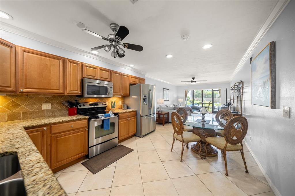 A kitchen with wood cabinets and granite countertops opens into a dining and living area — 5619 MIDNIGHT PASS ROAD UNIT 503, SARASOTA, FL