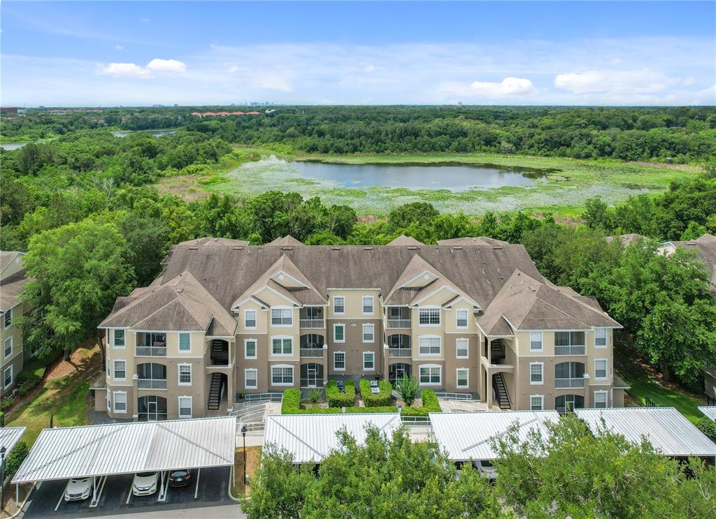 An aerial view shows a multi-story apartment building with covered parking and a nearby lake — 586 BRANTLEY TERRACE WAY UNIT 306, ALTAMONTE SPRINGS, FL
