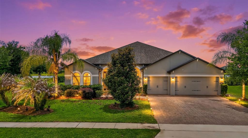 A single-story house with a paved driveway, three-car garage, and palm trees at sunset — 17614 SAILFIN DRIVE, ORLANDO, FL