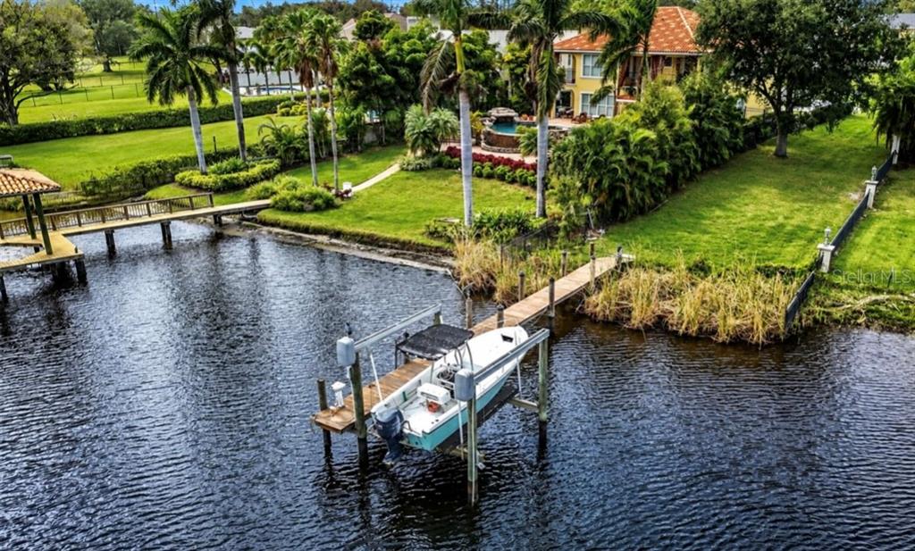 An aerial view of a waterfront property featuring a boat lift, dock, and landscaped yard — 4929 N RIVER SHORE DRIVE UNIT A, TAMPA, FL