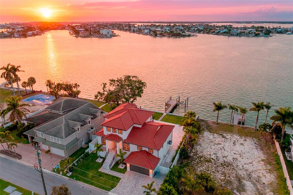 An aerial view shows a waterfront house with a red roof, dock, and palm trees — 4 PARADISE LANE, TREASURE ISLAND, FL