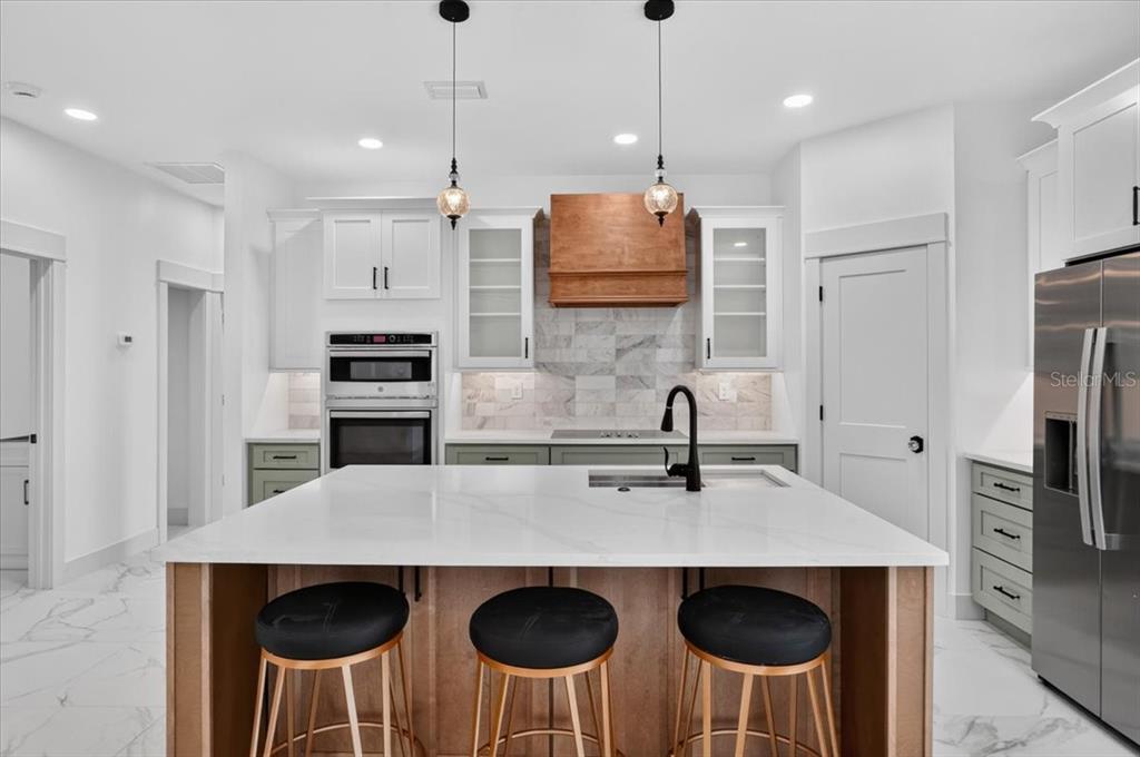 A modern kitchen features a white quartz island, wood-toned cabinetry, and a marble backsplash — 412 17TH AVENUE W, PALMETTO, FL