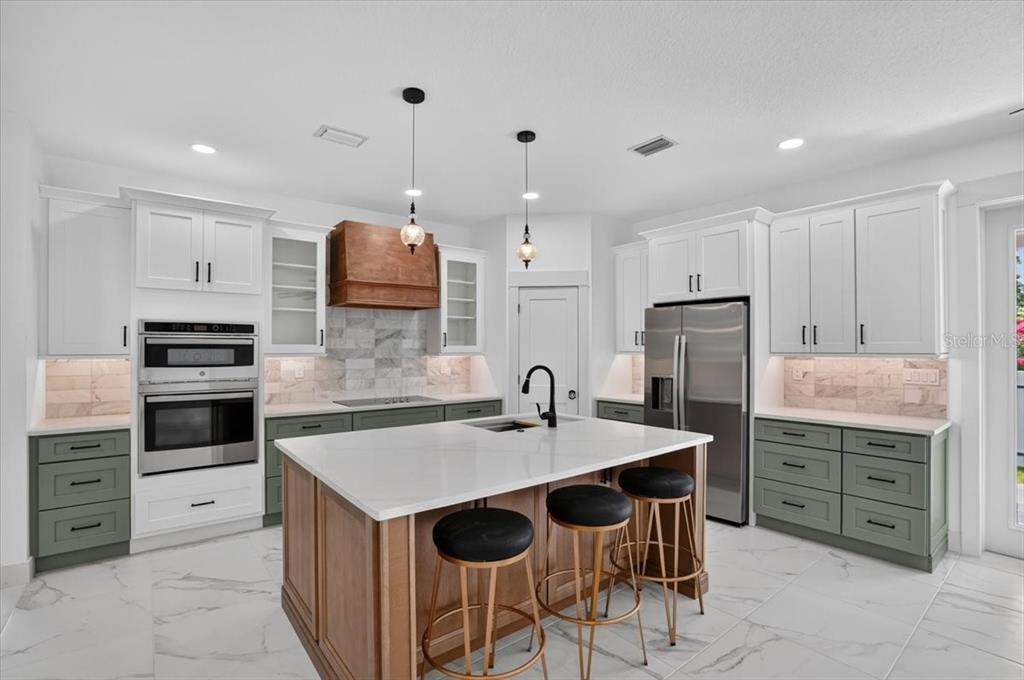 A modern kitchen features white upper cabinets, sage green lower cabinets, and a wood-toned island — 412 17TH AVENUE W, PALMETTO, FL