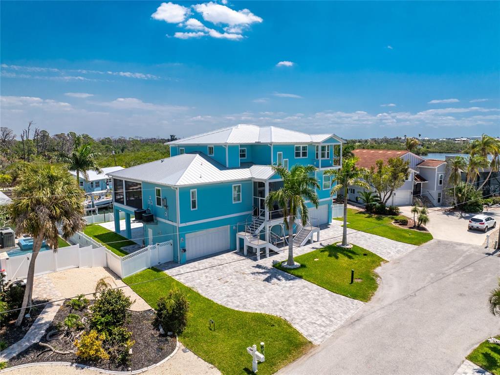 An aerial view of a bright blue, three-story coastal house with a metal roof — 9290 PINE COVE DRIVE, ENGLEWOOD, FL