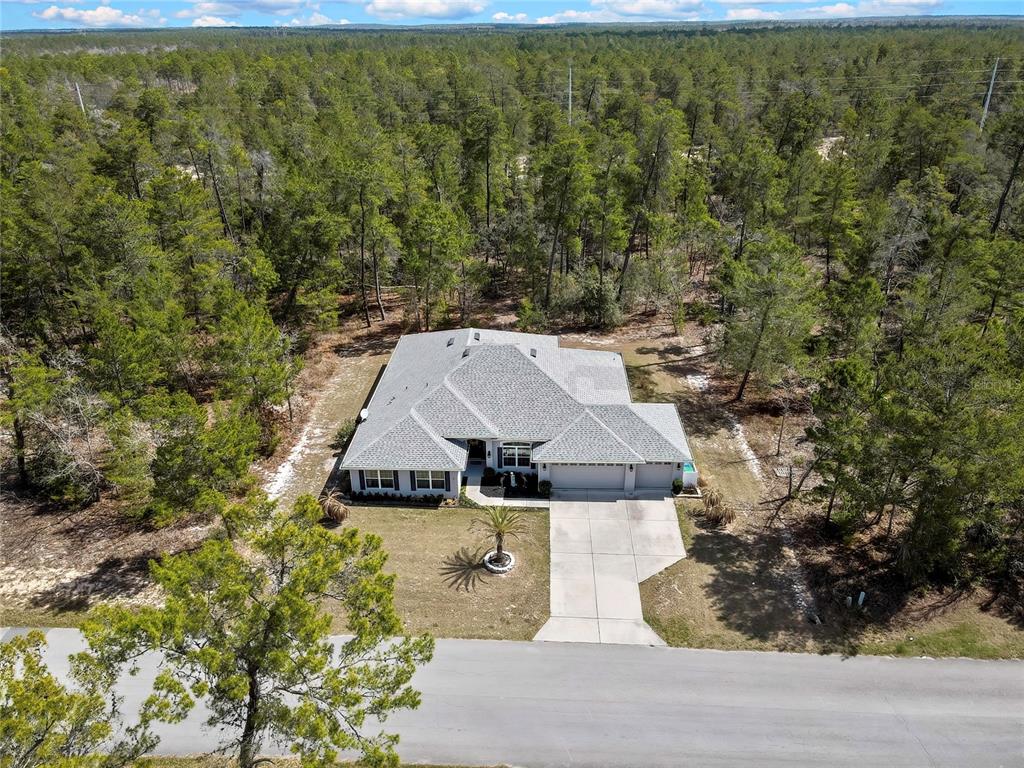 An aerial view shows a single-story house with a gray roof surrounded by dense forest — 24 TALL MARIGOLDS COURT, HOMOSASSA, FL