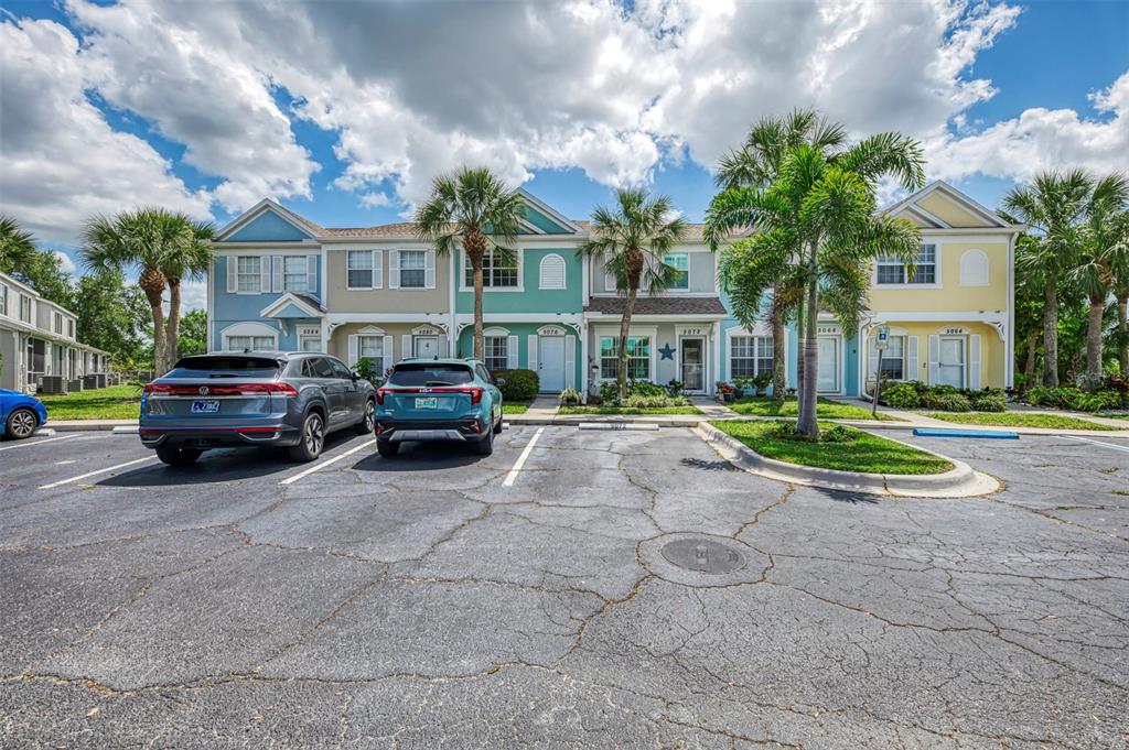 A row of colorful townhouses with palm trees and parked cars in the foreground — 5072 MISTY CANAL PLACE, BRADENTON, FL