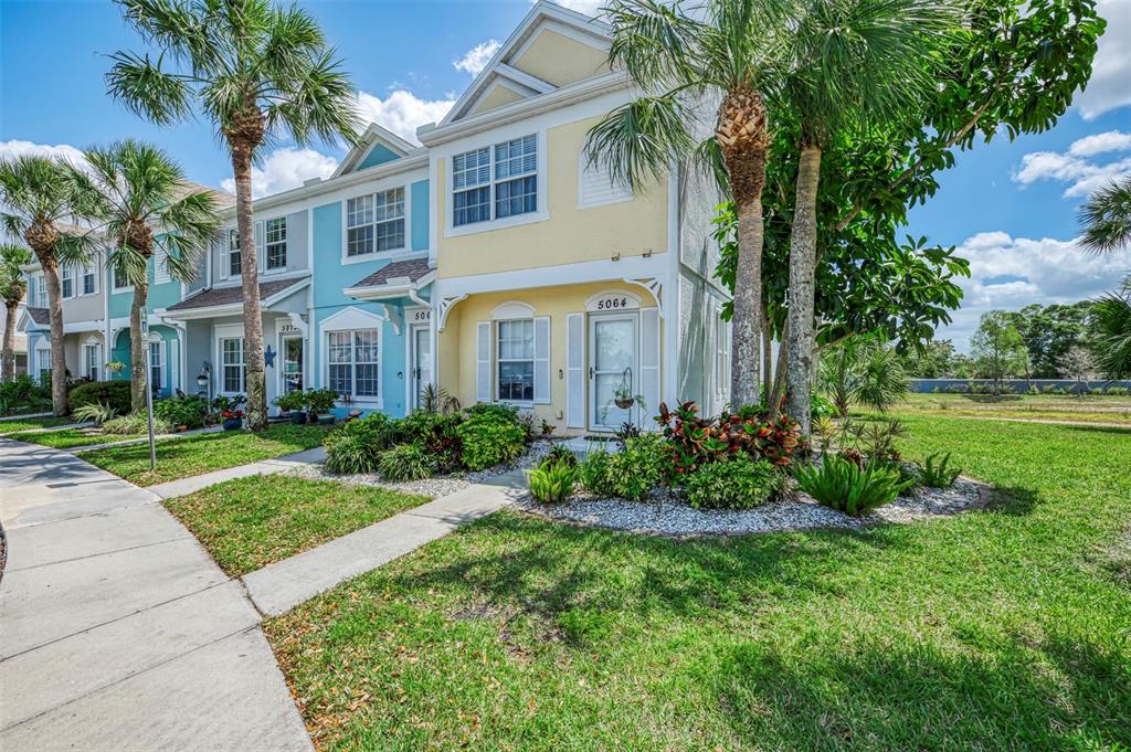 A two-story yellow townhouse with a front walkway and palm trees under a blue sky — 5072 MISTY CANAL PLACE, BRADENTON, FL
