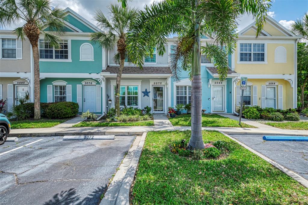 A row of colorful two-story townhouses with palm trees and a parking lot in front — 5072 MISTY CANAL PLACE, BRADENTON, FL