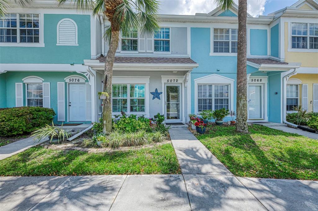 A row of three colorful townhouses features white doors, windows, and small front gardens — 5072 MISTY CANAL PLACE, BRADENTON, FL