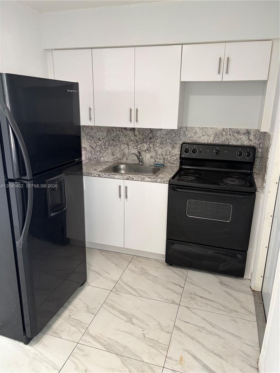 A small kitchen features white cabinets, black appliances, a sink, and light-colored tile flooring — 14399 NE 5th Pl # 5, North Miami FL 33161, NORTH MIAMI, FL