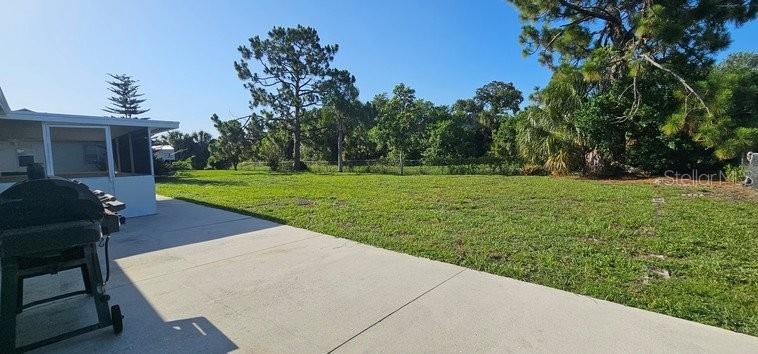 A concrete patio overlooks a large, grassy backyard with trees under a clear blue sky — 7855 W PRICE BOULEVARD, NORTH PORT, FL