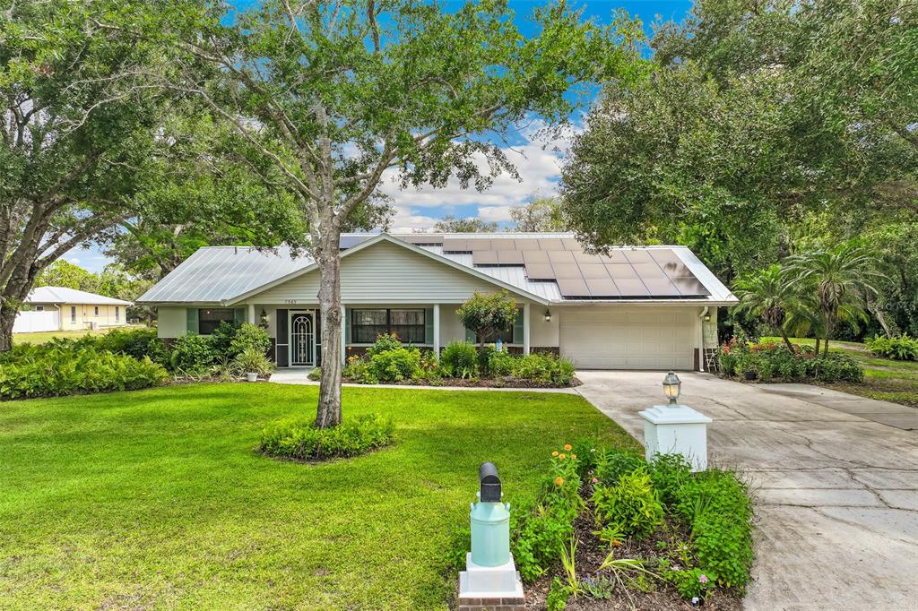 A single-story house with a metal roof, solar panels, and a front lawn with trees — 7565 CASTLE DRIVE, SARASOTA, FL