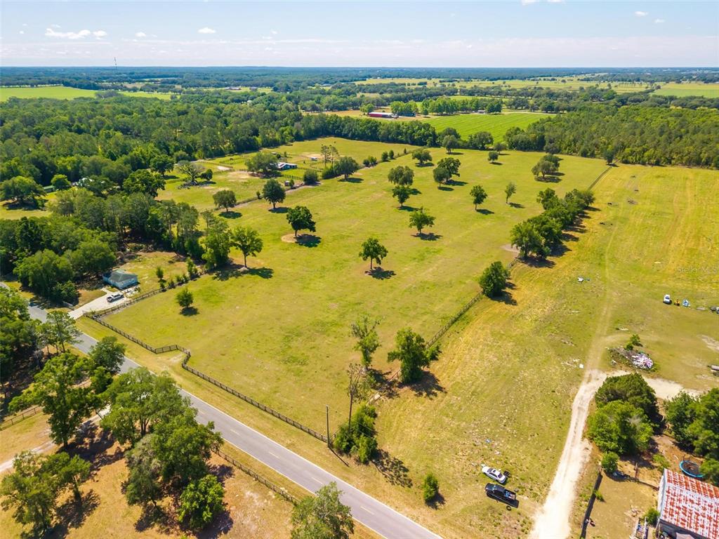 An aerial view shows a large, fenced grassy pasture dotted with trees along a road — TBD SE 42ND PLACE, MORRISTON, FL