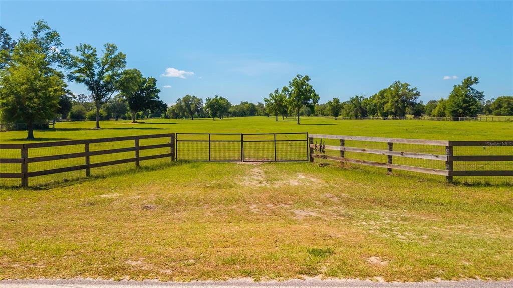 A fenced pasture with a metal gate and scattered trees under a clear blue sky — TBD SE 42ND PLACE, MORRISTON, FL