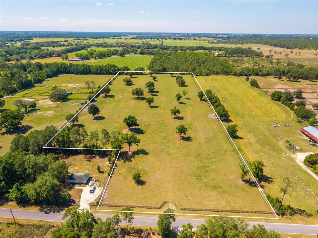 An aerial view shows a large, fenced grassy lot with scattered trees and a small house — TBD SE 42ND PLACE, MORRISTON, FL
