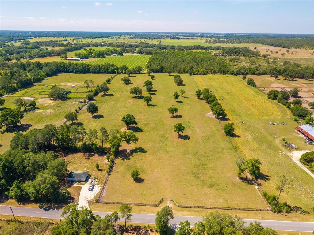 An aerial view shows a large, fenced grassy pasture with scattered trees and a house — TBD SE 42ND PLACE, MORRISTON, FL
