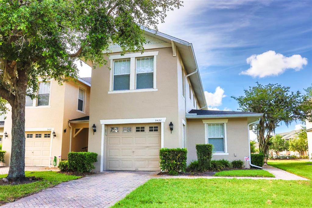 A two-story tan house with a single-car garage and a brick driveway — 5428 CARAMELLA DRIVE, ORLANDO, FL