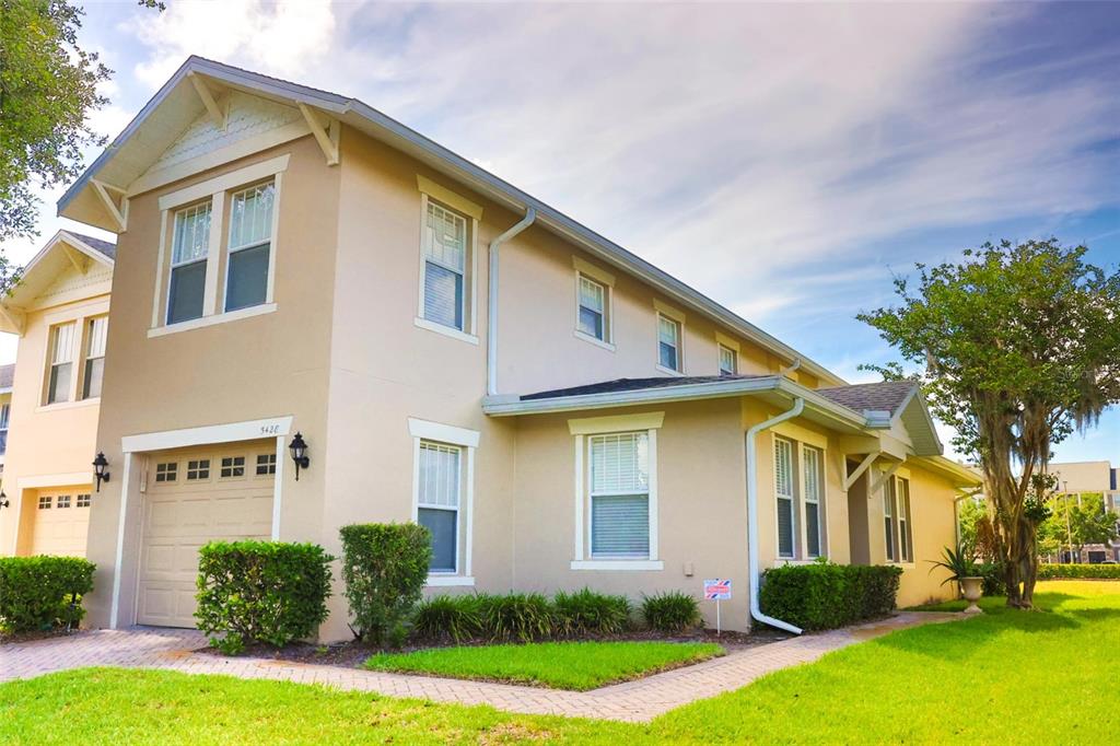 A two-story beige stucco house with a garage and a brick walkway on a lawn — 5428 CARAMELLA DRIVE, ORLANDO, FL