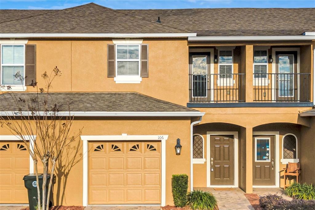 The exterior of a two-story townhouse features a tan stucco facade, garage, and balcony — 106 CARMICHAEL WAY, DAYTONA BEACH, FL