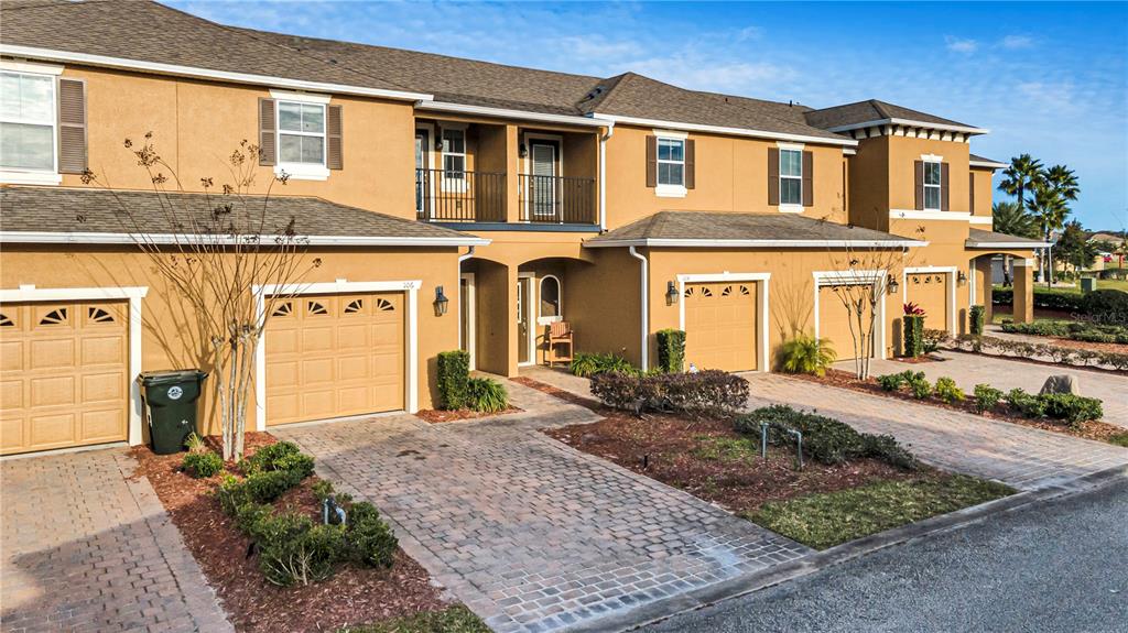 A row of tan townhouses with paved driveways, garage doors, and second-story balconies — 106 CARMICHAEL WAY, DAYTONA BEACH, FL