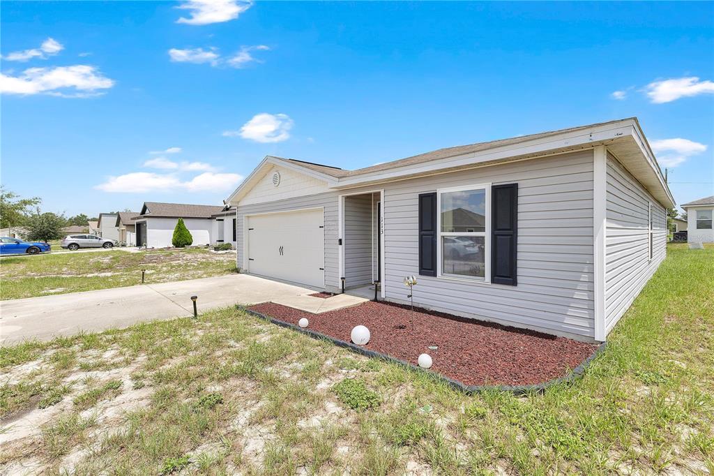 A single-story house with light gray siding, a two-car garage, and a red mulch garden — 113 TULIP LANE, KISSIMMEE, FL